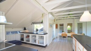 Cozinha com armários brancos, área de jantar com mesa e cadeiras, e luminária pendente.