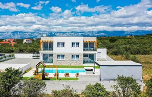 Ein modernes, zweistöckiges Haus mit Swimmingpool, Sitzgelegenheit im Freien und Blick auf die Berge.