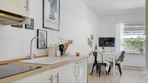 A modern kitchen with a sink, stove, and dining area with chairs and a TV. - Beautiful apartment in Nexø (Nexø)
