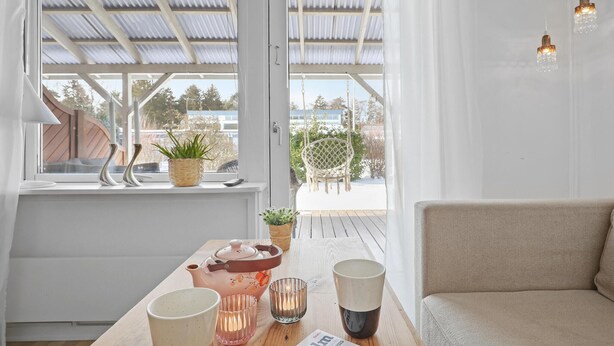 A cozy room with a wooden table, a sofa, a window with a view of greenery, and a hanging chair. - Beautiful apartment in Nexø (Nexø)