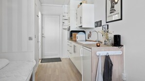 A compact kitchen with white cabinets, a sink, and a small countertop. There is a door leading to another room, a plant on the countertop, and a framed picture on the wall. - Beautiful apartment in Nexø (Nexø)