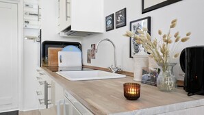 A modern kitchen with a white sink, stainless steel faucet, and a wooden countertop. There are framed pictures on the wall and a vase with dried flowers on the counter. - Beautiful apartment in Nexø (Nexø)