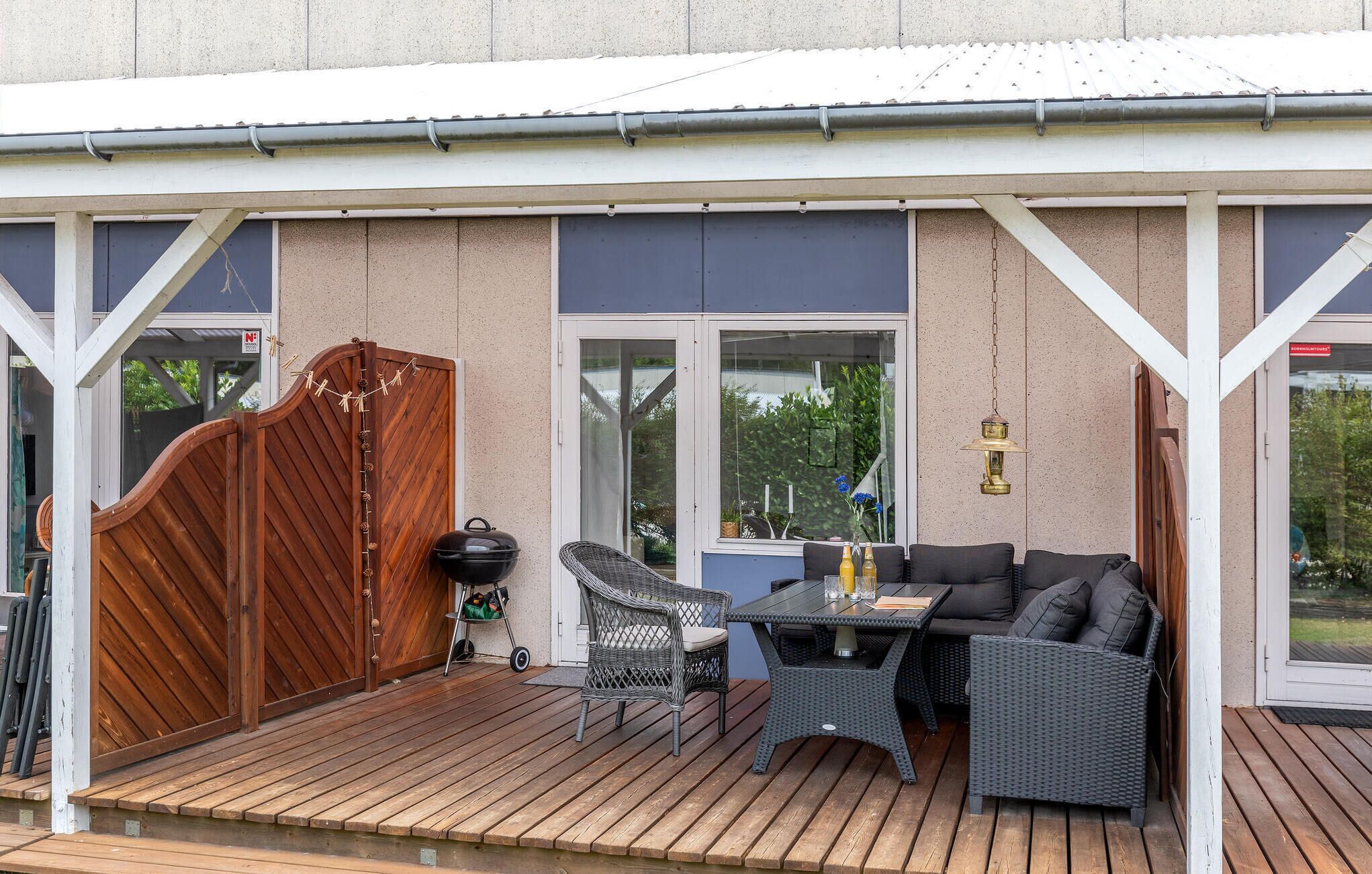 A covered outdoor patio with a wooden deck, wicker furniture, and a barbecue grill.
