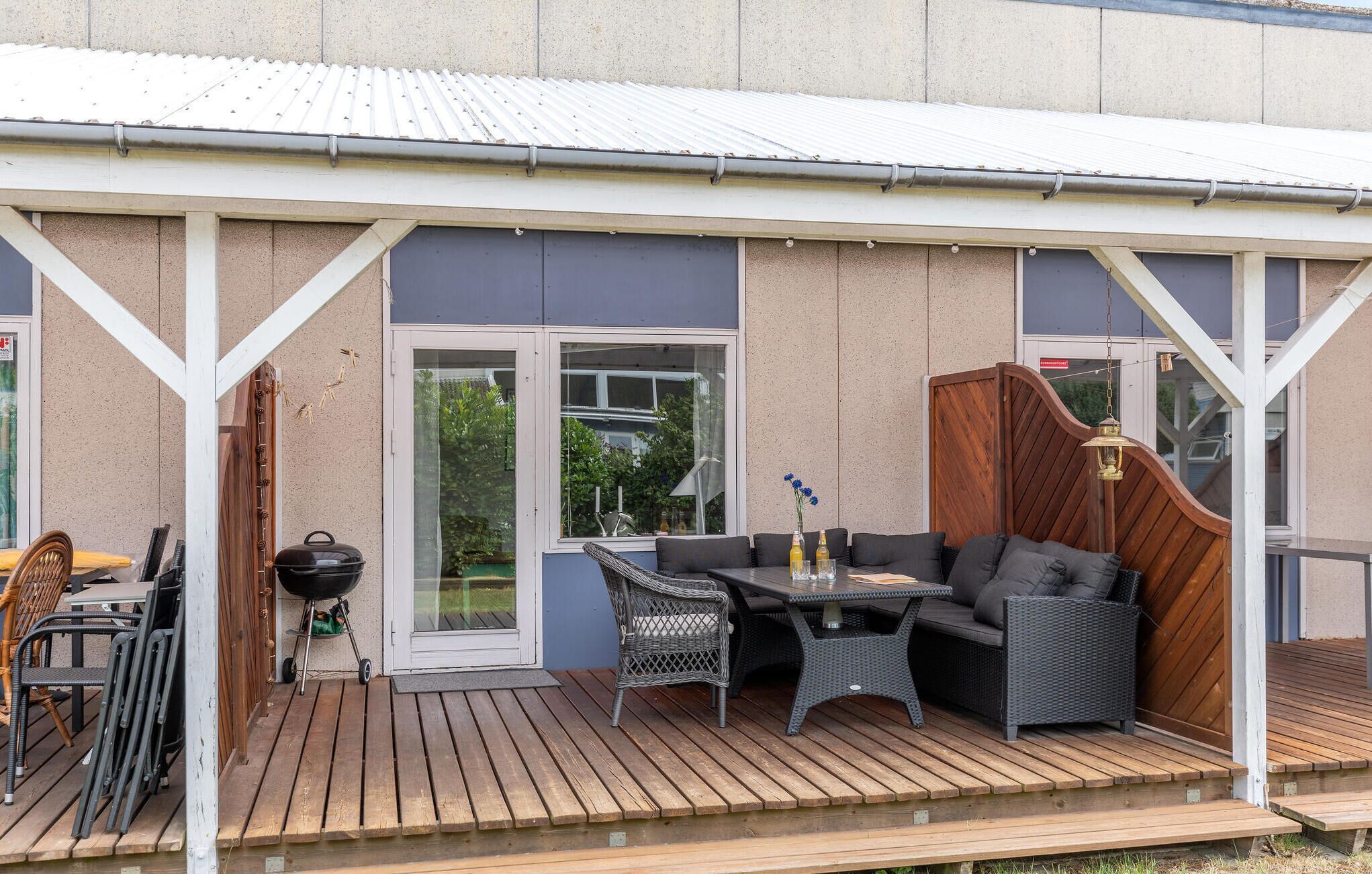 Eine Terrasse im Freien mit Holzdeck, Grill, Korbmöbeln und Blick ins grüne Umland.