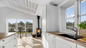 A modern kitchen with white cabinetry, a black stove, and a large window offering a view of the outdoors. - Awesome home in Blåvand with sauna (Blåvand)