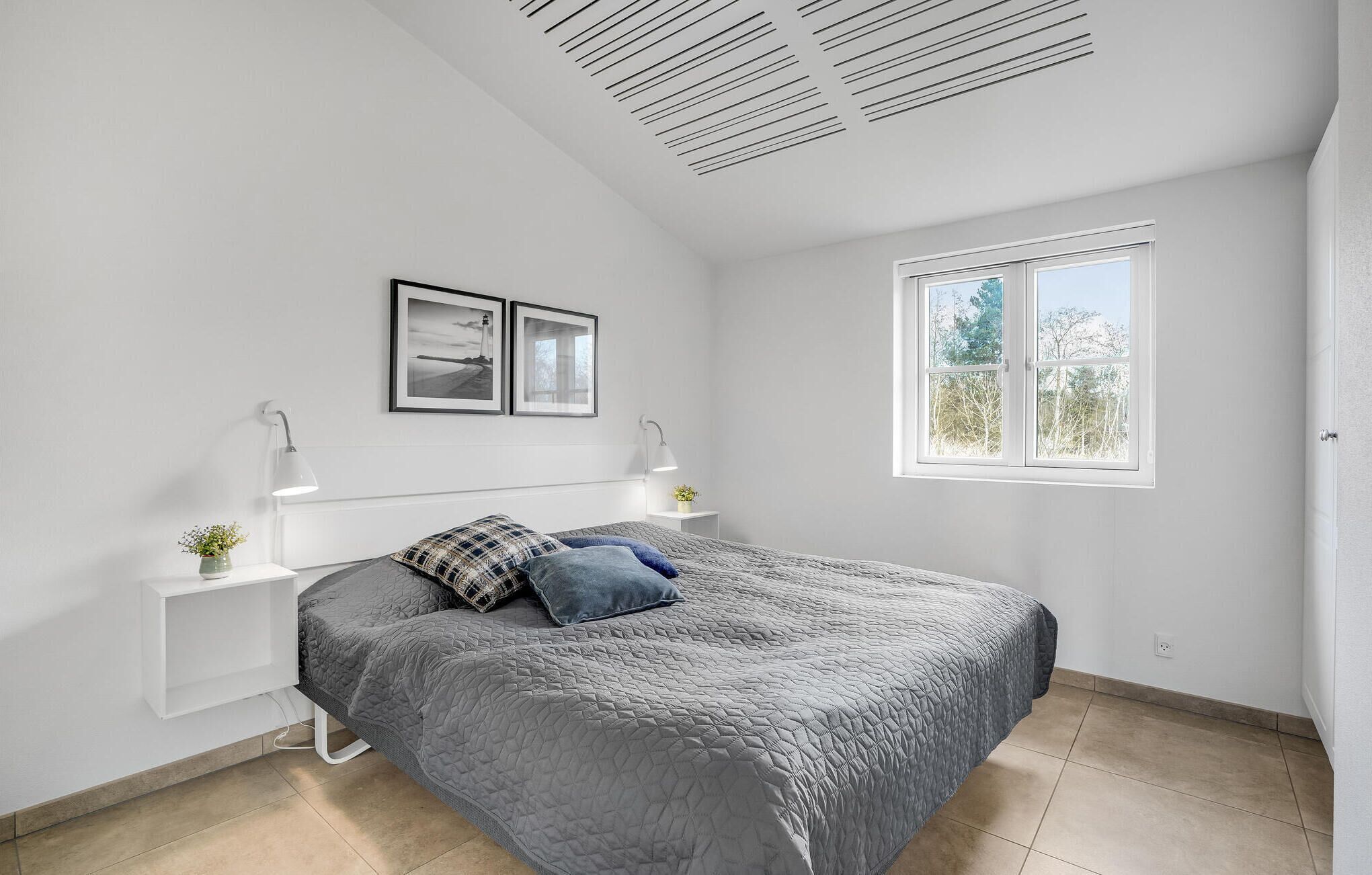 Ein Schlafzimmer mit einem Bett, zwei Nachttischen, einem Fenster und einer Decke mit Lüftung.