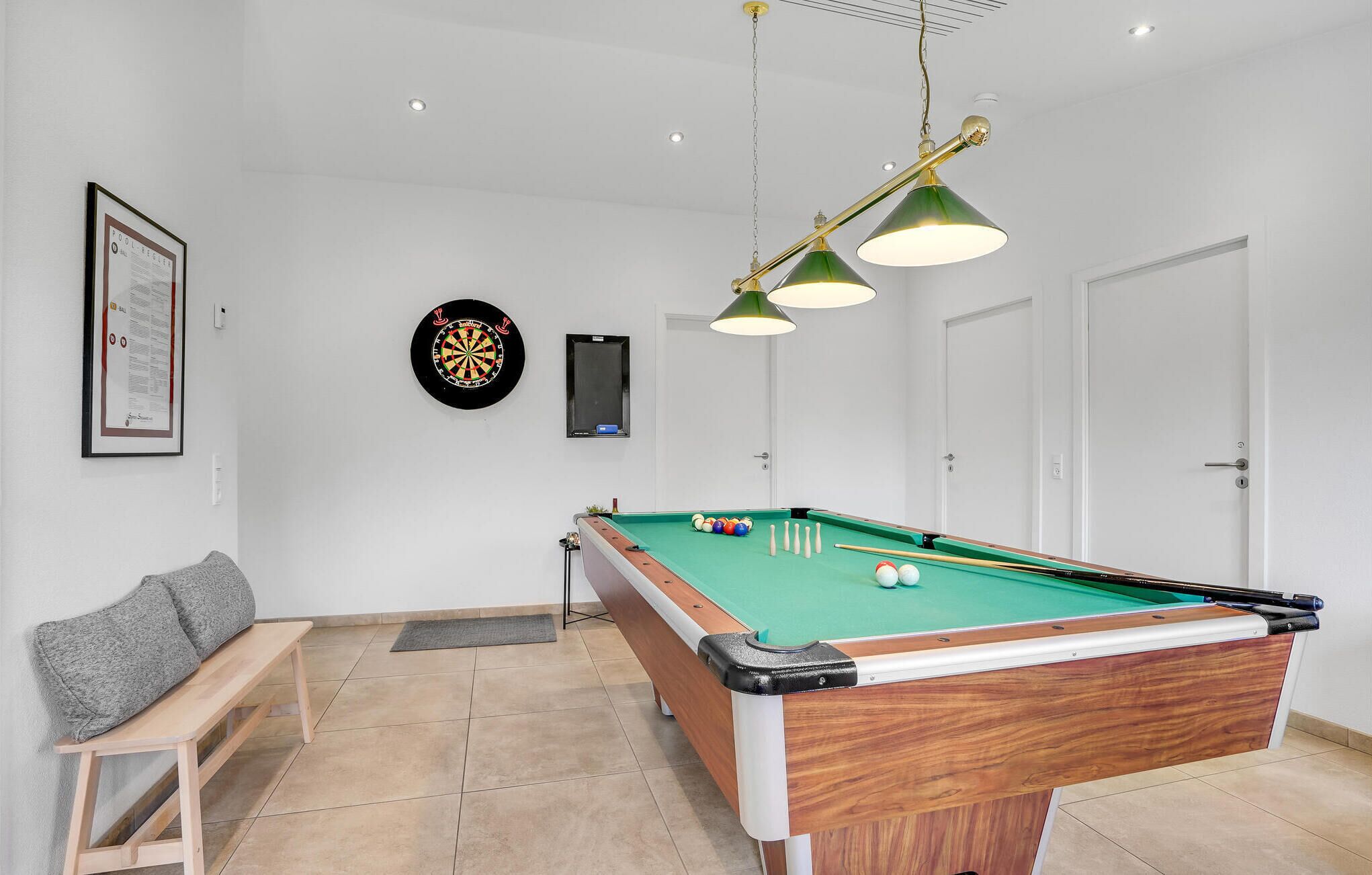 Una mesa de billar con superficie de fieltro verde, un banco de madera y un dardo en la pared.