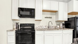 Une cuisine avec des meubles blancs, une cuisinière noire, un four à micro-ondes et un réfrigérateur.