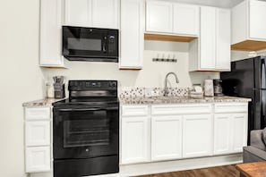 A kitchen with white cabinets, a black stove, a microwave, and a refrigerator. - Lavender - Private Getaway with Horseshoes, Stargazing, and Walking Trails (Wimberley)