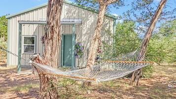 A hammock tied between two trees in a backyard with a shed in the background.