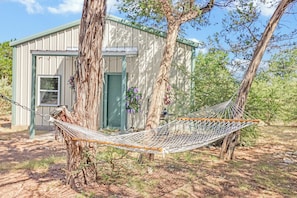 A hammock tied between two trees in a backyard with a shed in the background.