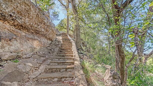 Un escalier en pierre menant au sommet d’une colline rocheuse, entouré d’arbres et de végétation.
