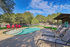 A swimming pool with a fountain, surrounded by red chairs and lounge chairs, with a wooden cabin in the background.