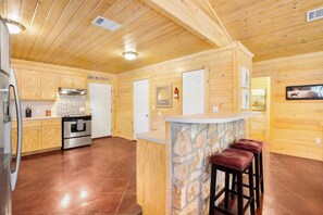 A wooden interior with a kitchen, a stone accent wall, and a bar area with stools.