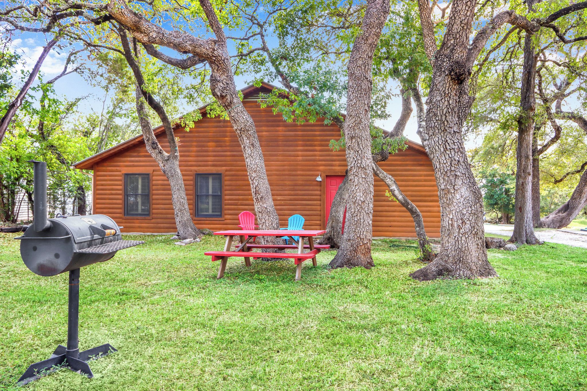 A wooden cabin with a picnic table and chairs, surrounded by trees.