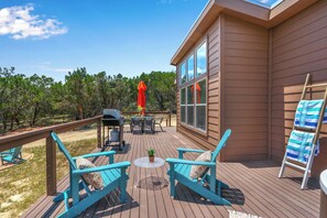 A wooden deck with outdoor furniture, a barbecue grill, and a view of trees.