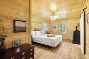 A wooden cabin bedroom with a bed, a nightstand, a dresser, and a ceiling fan. - The Oak Lodge - 3 Bedroom Cabin with Swimming Pool Access! Close to Downtown (Wimberley)