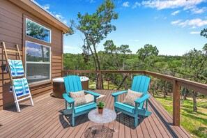 Une terrasse en bois avec deux chaises Adirondack bleues, une petite table avec une plante et une échelle appuyée contre un bâtiment.