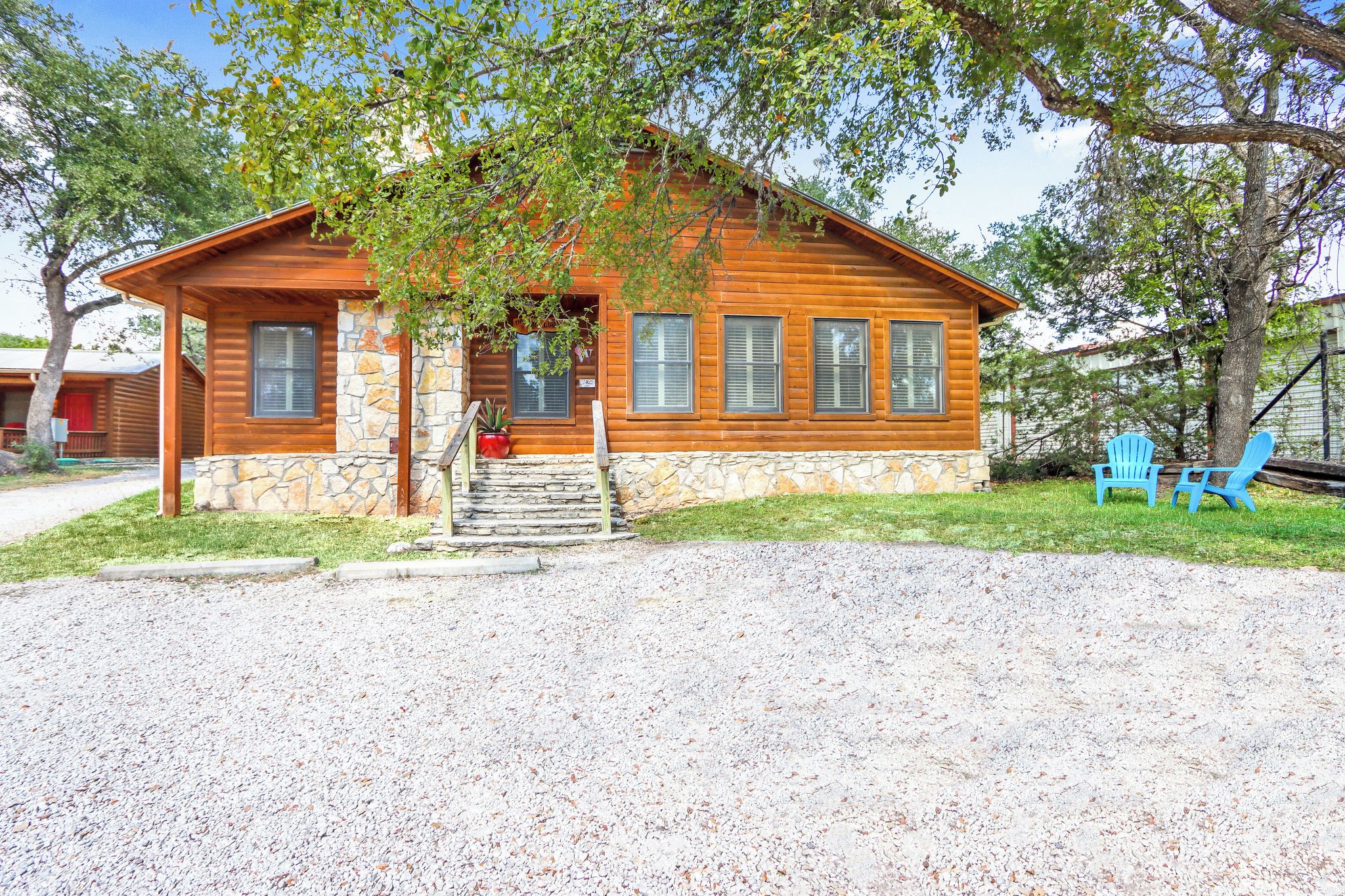 A wooden cabin with a stone foundation, a porch, and a gravel driveway.