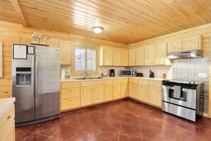 A kitchen with wooden cabinets, a stainless steel refrigerator, a microwave, and a stove. - The Oak Lodge - 3 Bedroom Cabin with Swimming Pool Access! Close to Downtown (Wimberley)