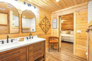 Une salle de bain de style rustique, avec des murs en bois, un grand miroir, deux lavabos et un meuble-lavabo doté de tiroirs.