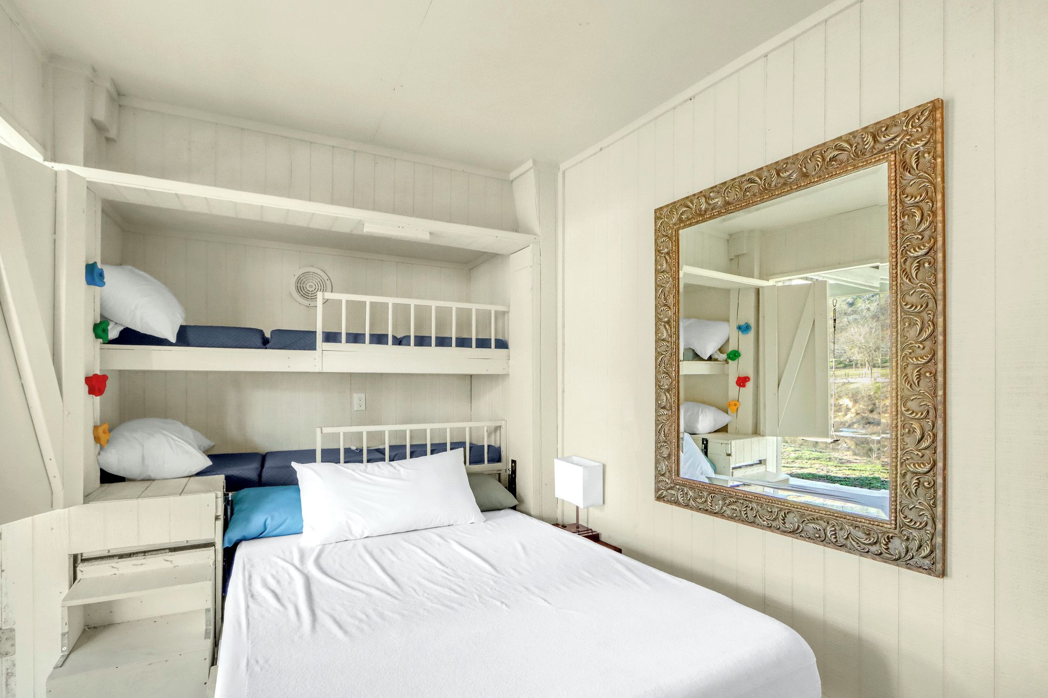 Une chambre avec un lit superposé, un grand miroir et une lampe de chevet.