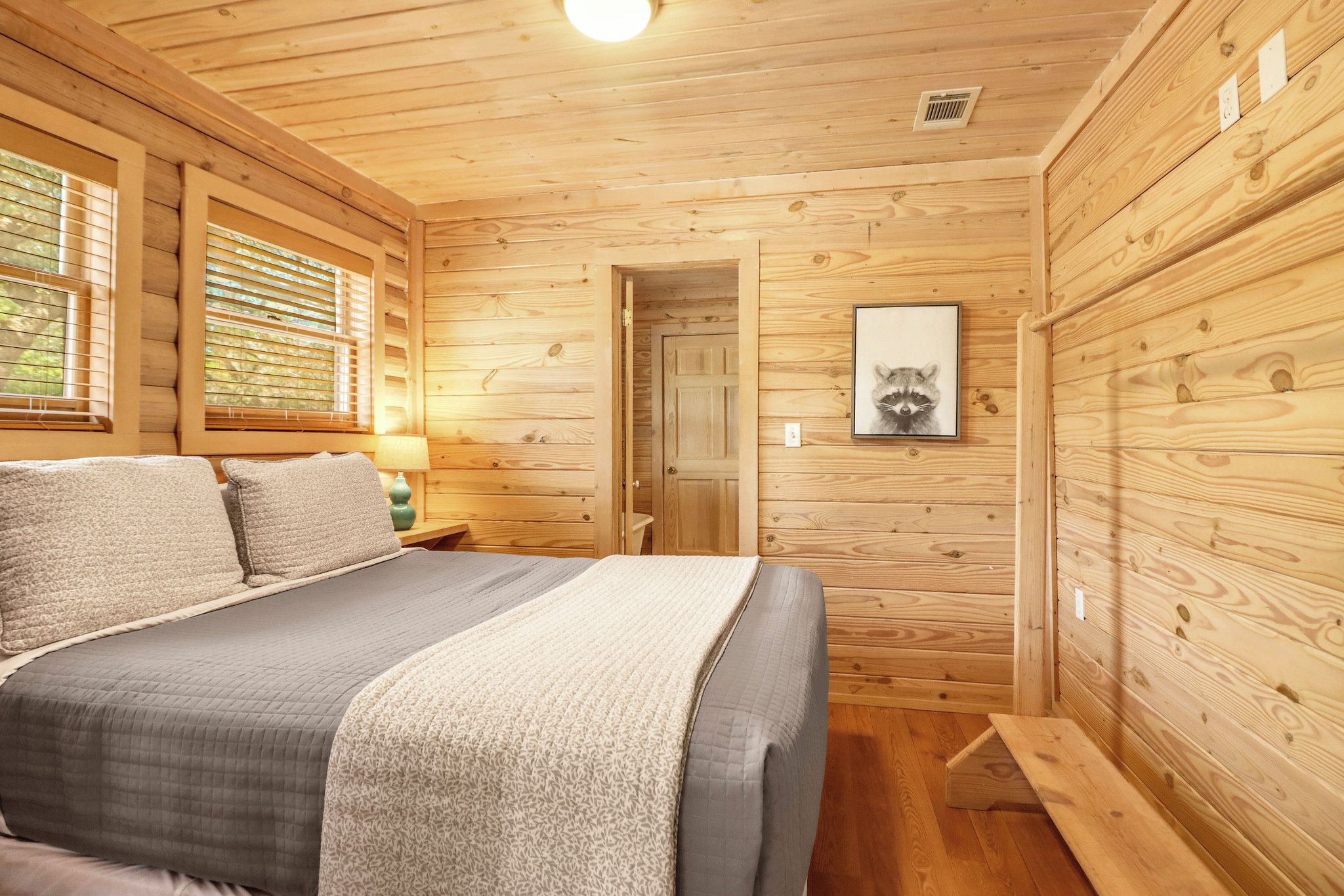 A wooden cabin bedroom with a bed, a nightstand, a lamp, and a framed picture on the wall.