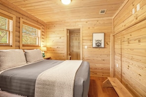 A wooden cabin bedroom with a bed, a nightstand, a lamp, and a framed picture on the wall.