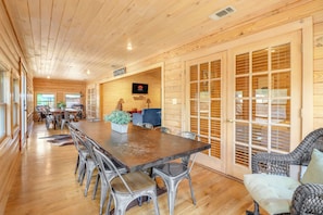 A spacious wooden interior with a long dining table, multiple chairs, a television, and a sign that reads 'GATHER'.