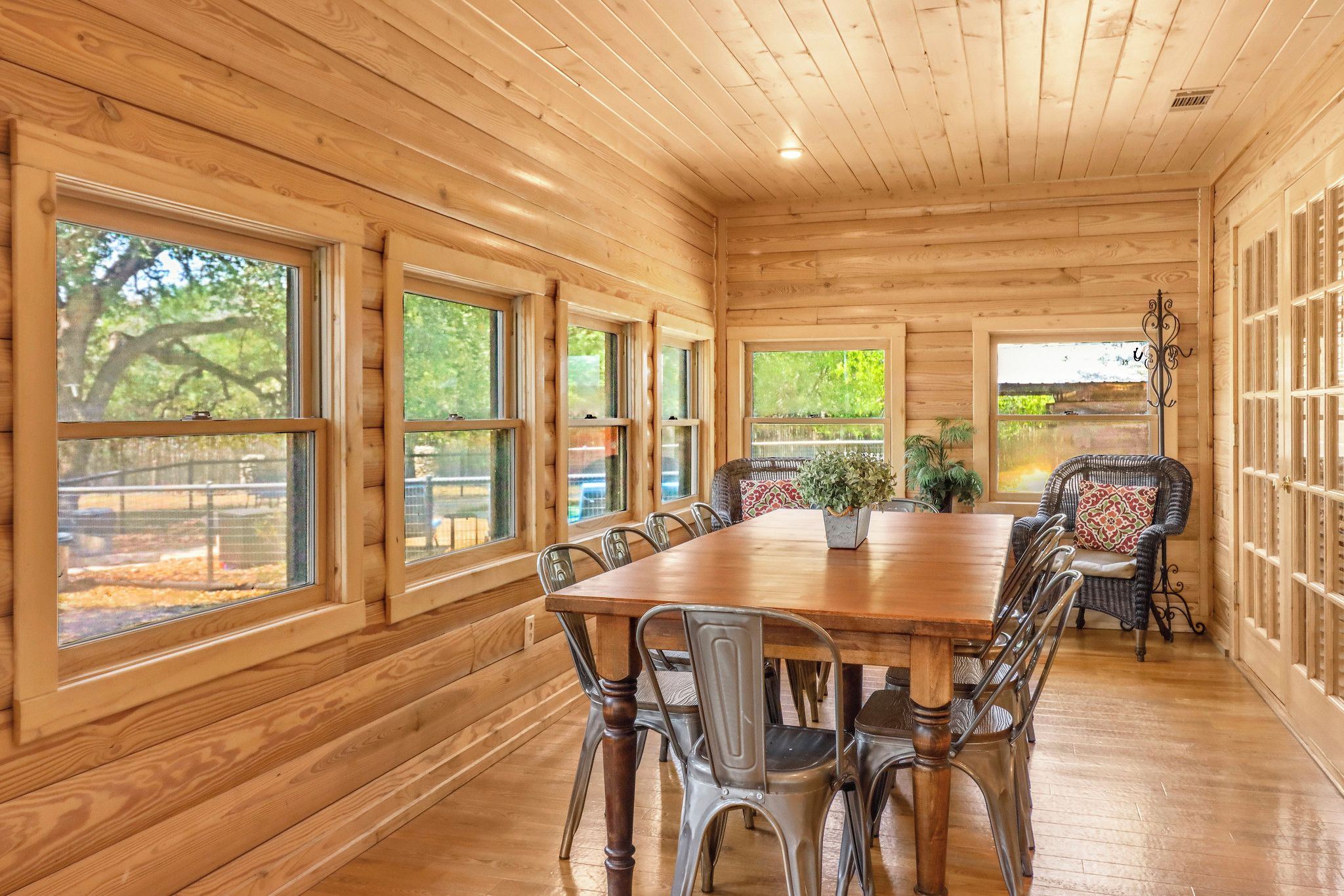 Een houten interieur met een eettafel en stoelen, grote ramen en uitzicht op het landschap.