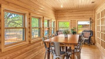 Een houten interieur met een eettafel en stoelen, grote ramen en uitzicht op het landschap.