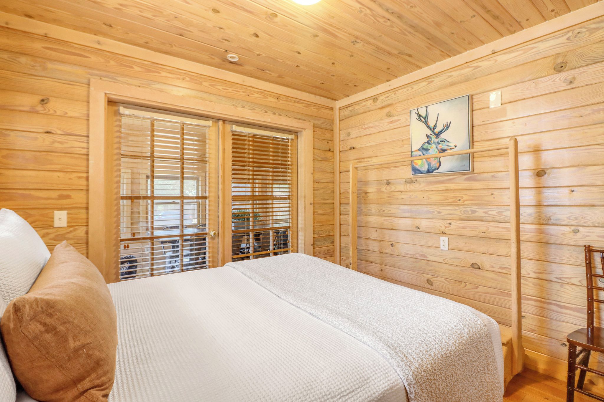 A wooden-paneled room with a bed, a window with blinds, and a painting on the wall.