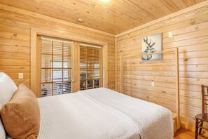 A wooden-paneled room with a bed, a window with blinds, and a painting on the wall. - Reunion Cabin - 2 Bedroom Cabin, Resort Pool, Commercial kitchen (Wimberley)