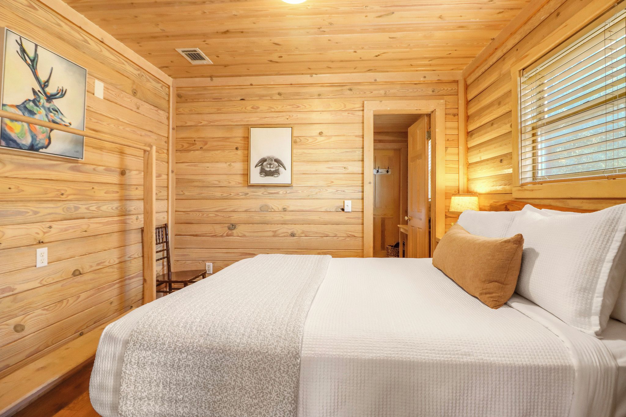 Ein Schlafzimmer einer Holzhütte mit einem Bett, einem Bilderrahmen mit einem Reh und einer Lampe.