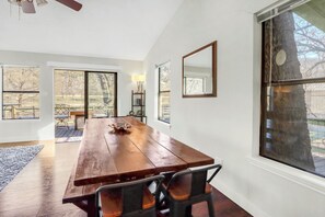 Un comedor con una mesa y sillas de madera, ventanas grandes y vistas al exterior.