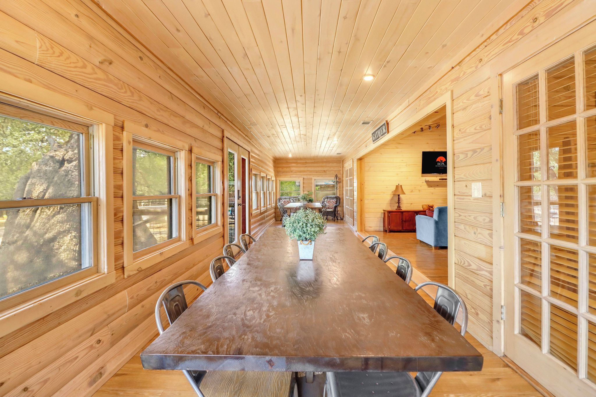 Ein langer Holztisch mit Stühlen, einer Topfpflanze und einem Fernseher an der Wand.