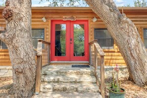 Una cabaña de madera con puerta roja, escalones de piedra y barandilla metálica.