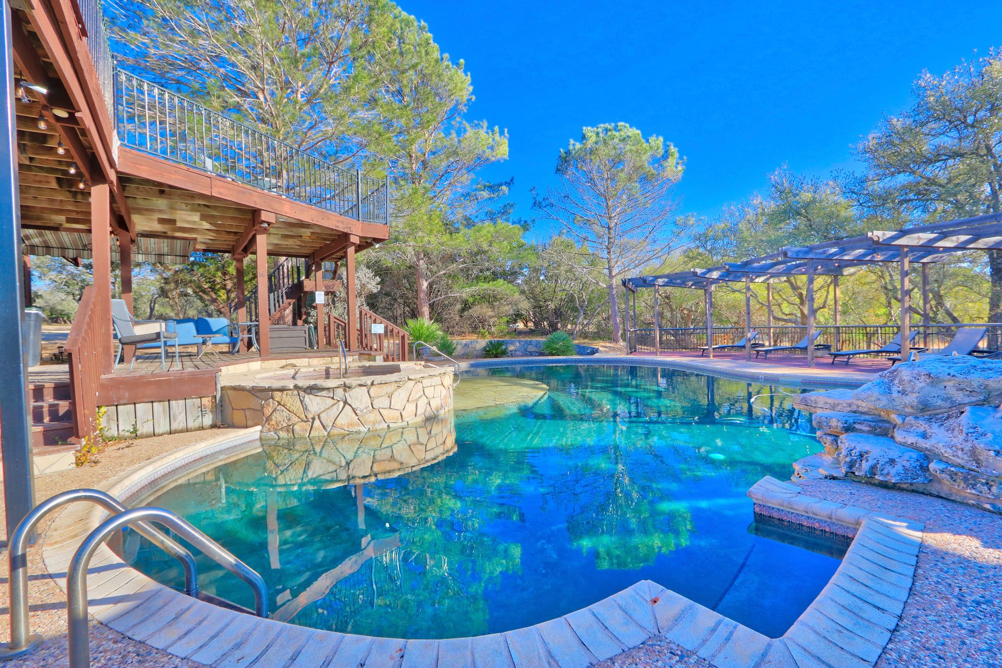 A swimming pool with a stone deck, wooden pergola, and outdoor seating area.