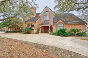 A brick house with a gabled roof, arched windows, and a front entrance. - Four Bedroom Ranch House with Swimming Pool Access on 75 Acres (Wimberley)