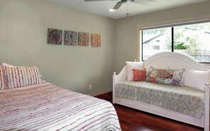 Un dormitorio con cama, una cama tipo sofá, ventilador de techo y ventana con vistas al exterior.
