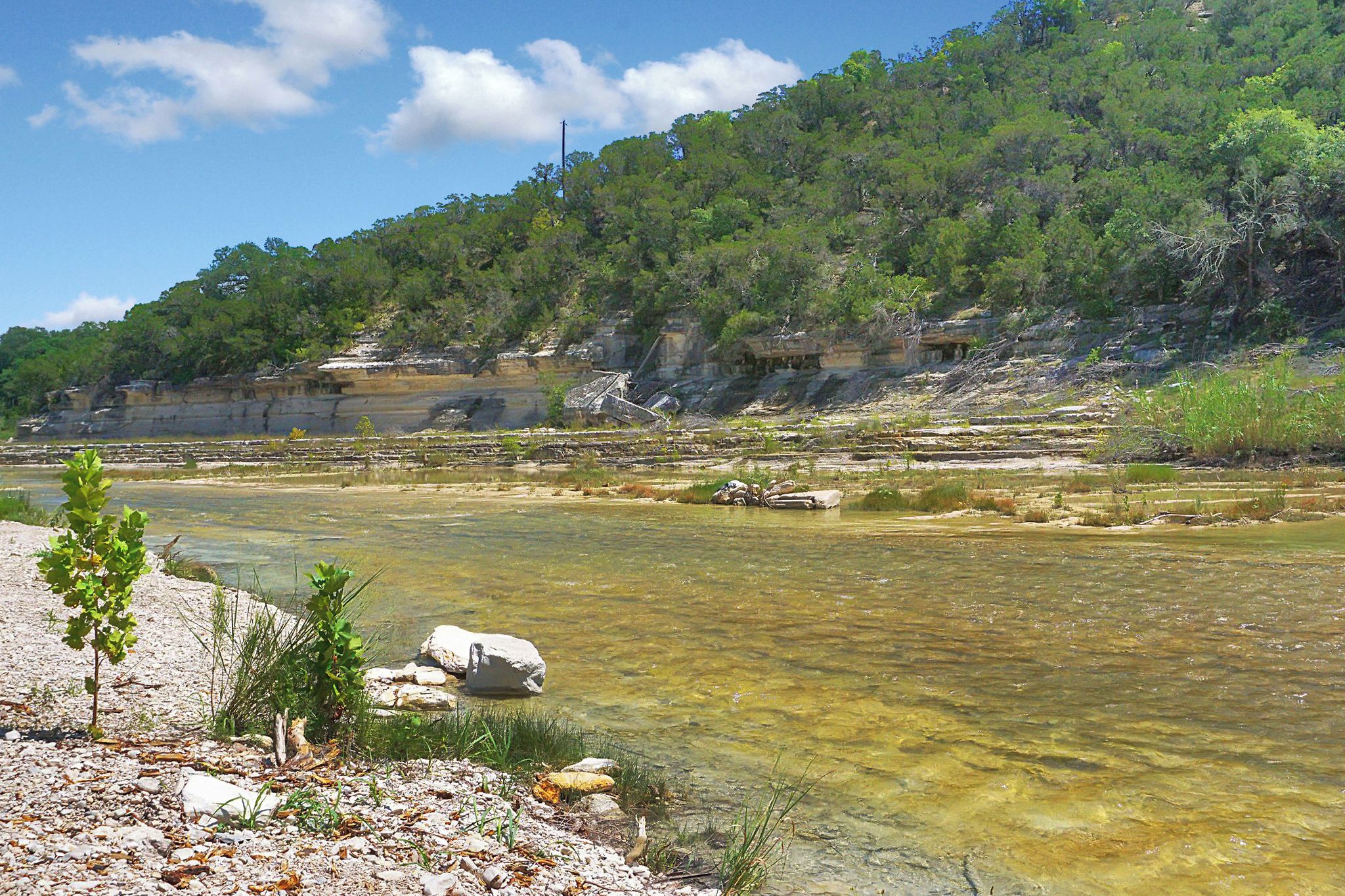 Un paisaje natural con un río cristalino, terreno rocoso y una colina arbolada.