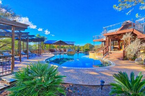 A pool area with lounge chairs, a covered seating area, and a building with a balcony. - Four Bedroom Ranch House with Swimming Pool Access on 75 Acres (Wimberley)