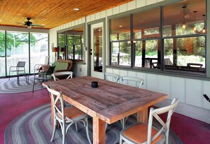 Una mesa de comedor de madera con sillas, ventanas amplias y un ventilador de techo.