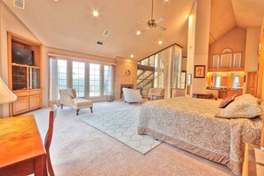 A spacious bedroom with a large bed, a desk, and a chair. There is a staircase leading to an upper level, and a large window providing natural light. - Four Bedroom Ranch House with Swimming Pool Access on 75 Acres (Wimberley)