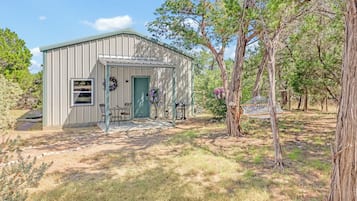 A small metal building with a door, windows, and a porch with chairs.