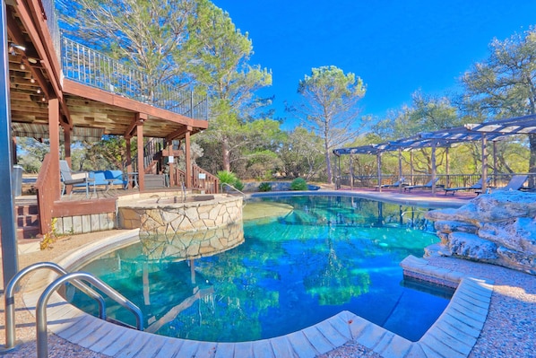 A swimming pool with a stone deck, wooden pergola, and outdoor seating area.