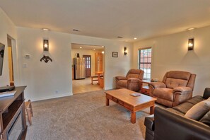 A spacious living room with a sofa, armchair, and coffee table. There is a kitchen area visible in the background. - Caretaker's Cottage with Swimming Pool Access on a 75 Acre Ranch (Wimberley)