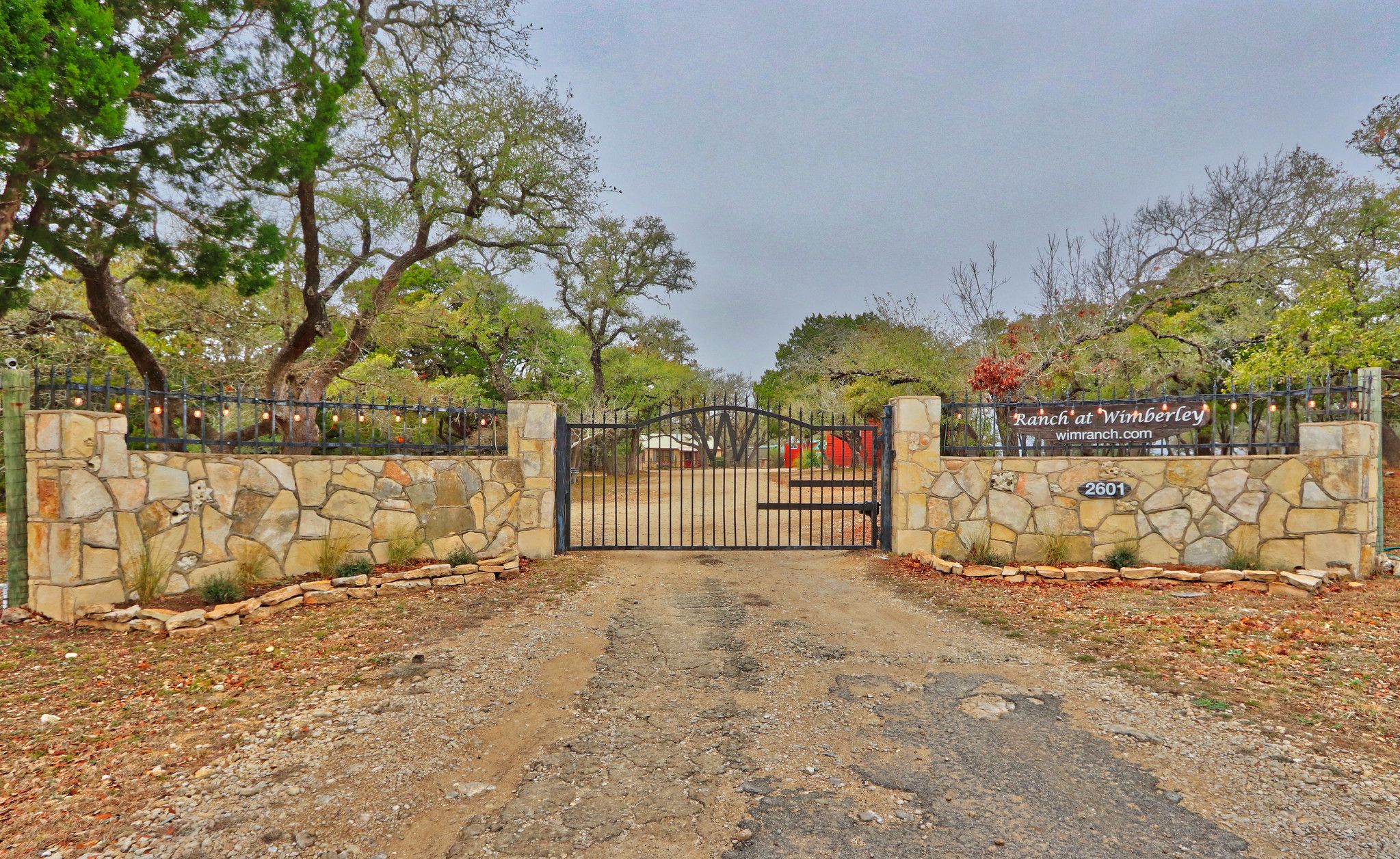 A gated entrance to a property with a stone wall and a metal gate.