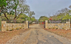 A gated entrance to a property with a stone wall and a metal gate. - Caretaker's Cottage with Swimming Pool Access on a 75 Acre Ranch (Wimberley)