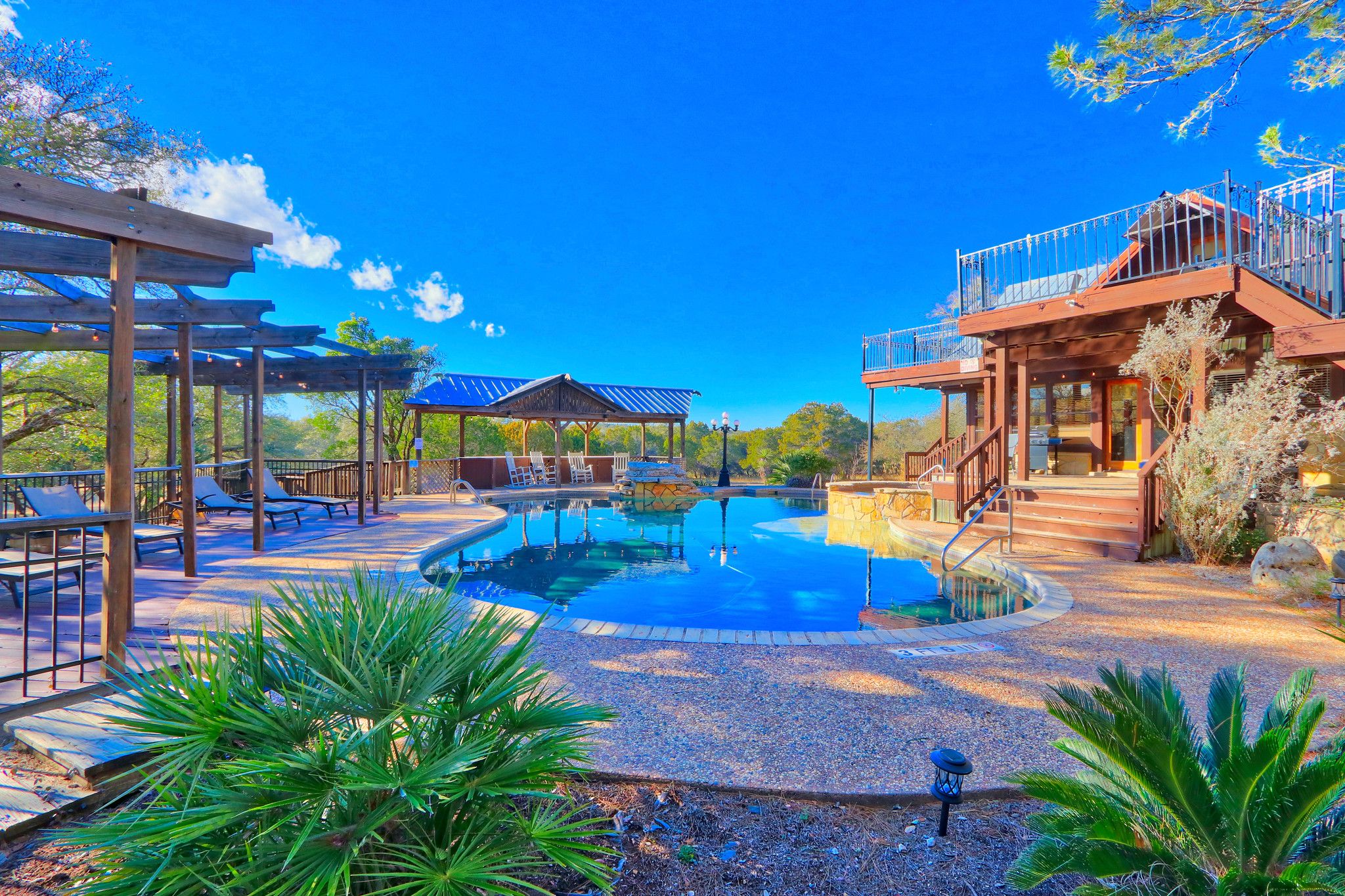 A pool area with lounge chairs, a covered seating area, and a building with a balcony.